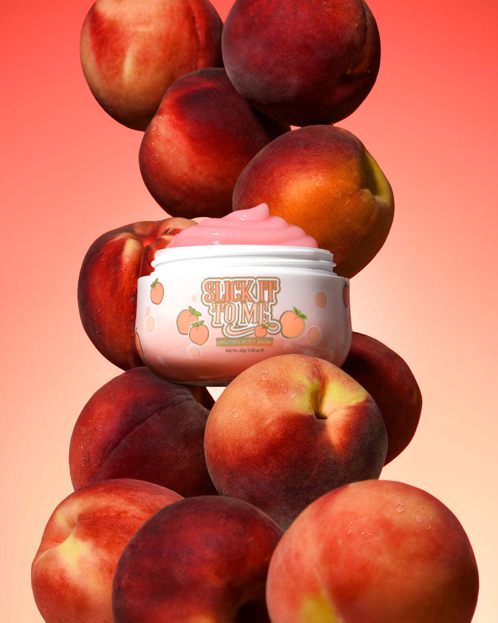 Jar of P. Louise Slick It To Me Peach Melting Body Balm s růžovým krémem obklopeným broskvemi na gradientním pozadí