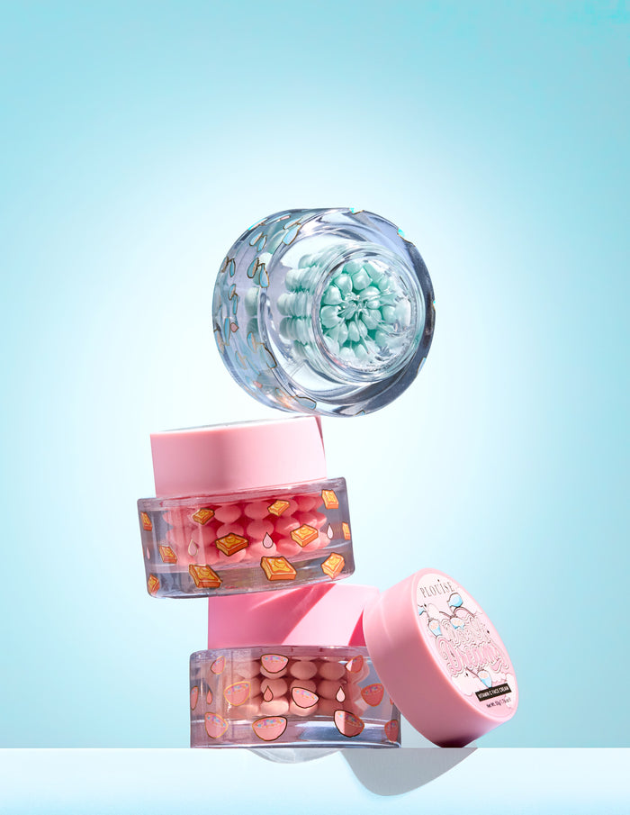 Tři malé sklenice s barevnými kapslemi vitamínu C v gelu na světle modrém pozadí