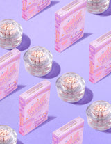 Průhledné nádobky P.Louise DOse of Dreams Viatmin C Capsule Face Cream s růžovými kapslemi v nich obklopenými růžovými cereáliemi na fialovém pozadí