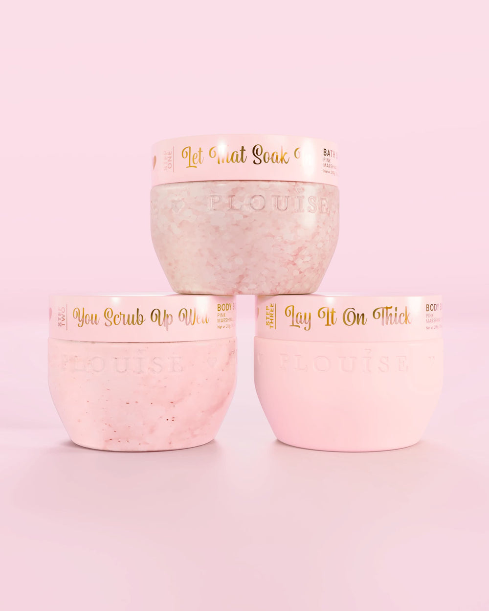 Three P.Louise Hop Into Self-Care Pink Marshmallow pink containers featuring bath salts, body scrub and body butter with gold text on a pink background