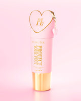 Obří růžová a zlatá láhev Protect Your Pout s uzávěrem ve tvaru srdce na světle růžovém pozadí