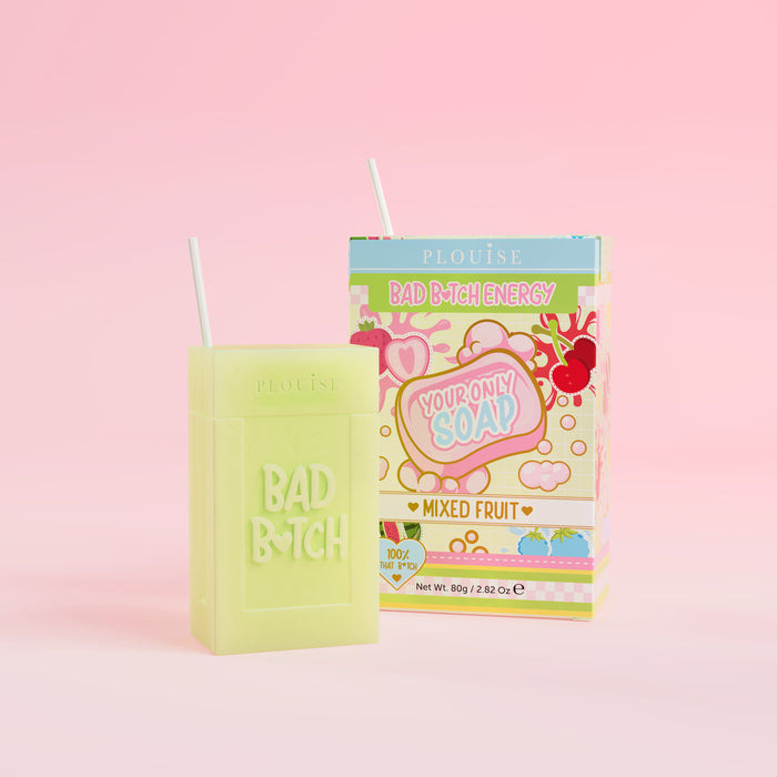 Zelené mýdlo s vyrytým nápisem „Bad Bitch“ spolu s barevným balením krabičky od džusu s nápisem „Mixed Fruit“ na růžovém pozadí.