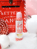 Láhev P. Louise Ready Set Sparkle Christmas Glitter Setting Spray obklopená svátečními dekoracemi, jako je sníh, ozdoby a vánoční poštovní schránka