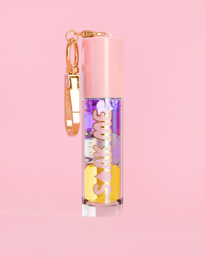 P. Louise Soak Me Lip Oil s barevným vrstveným olejem v růžové tubě se zlatou sponou na růžovém pozadí