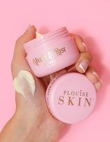 Osoba, která drží růžovou nádobu s očním krémem P.Louise Give It A Rest se staženým víčkem a na nádobce ukazuje název produktu a značku.